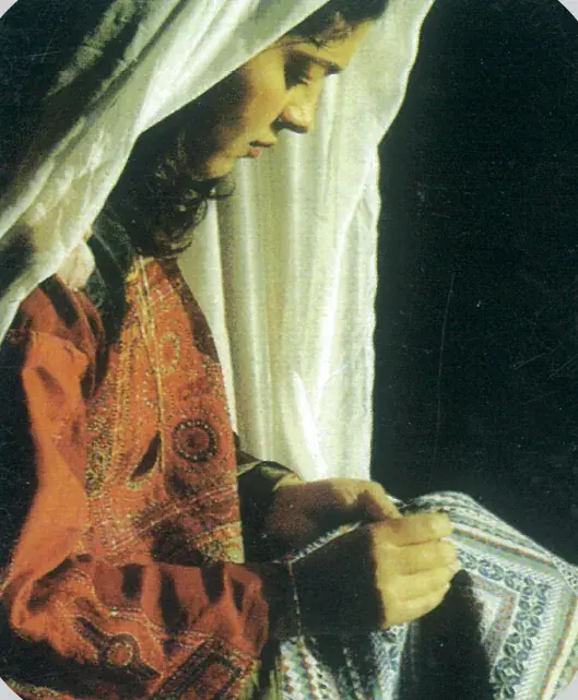 A woman in an embroidered thobe working on tatreez